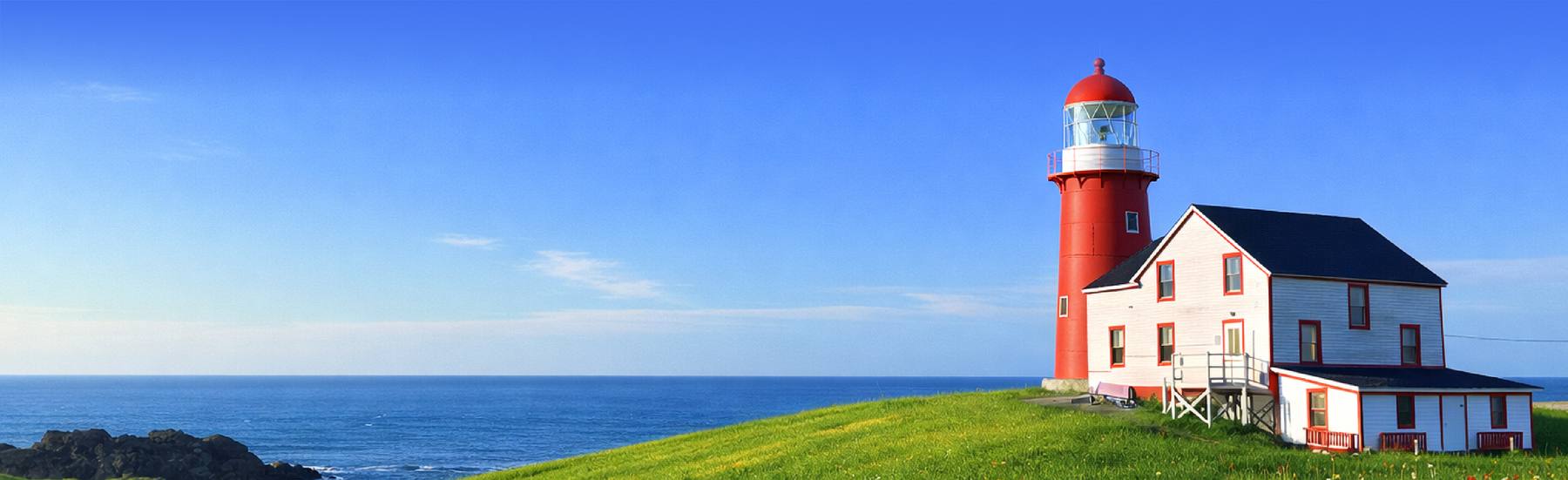 The red Ferryland lighthouse and white house on a green headland above the Atlantic